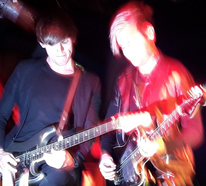 blurry photo of kier kemp and another guy playing guitar
