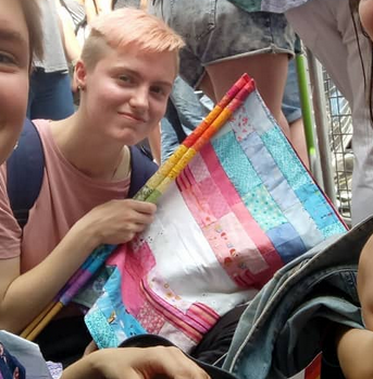 jay holding a patchwork trans flag and smiling