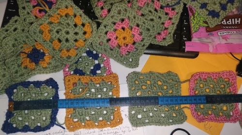 Granny square crocheted patches in green, blue, pink and yellow next to a blue measuring tape.