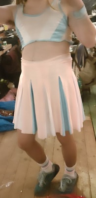 cropped headless mirror selfie of white drag queen wearing pale blue, pink and white crop top, pleated skirt and blue shoes.