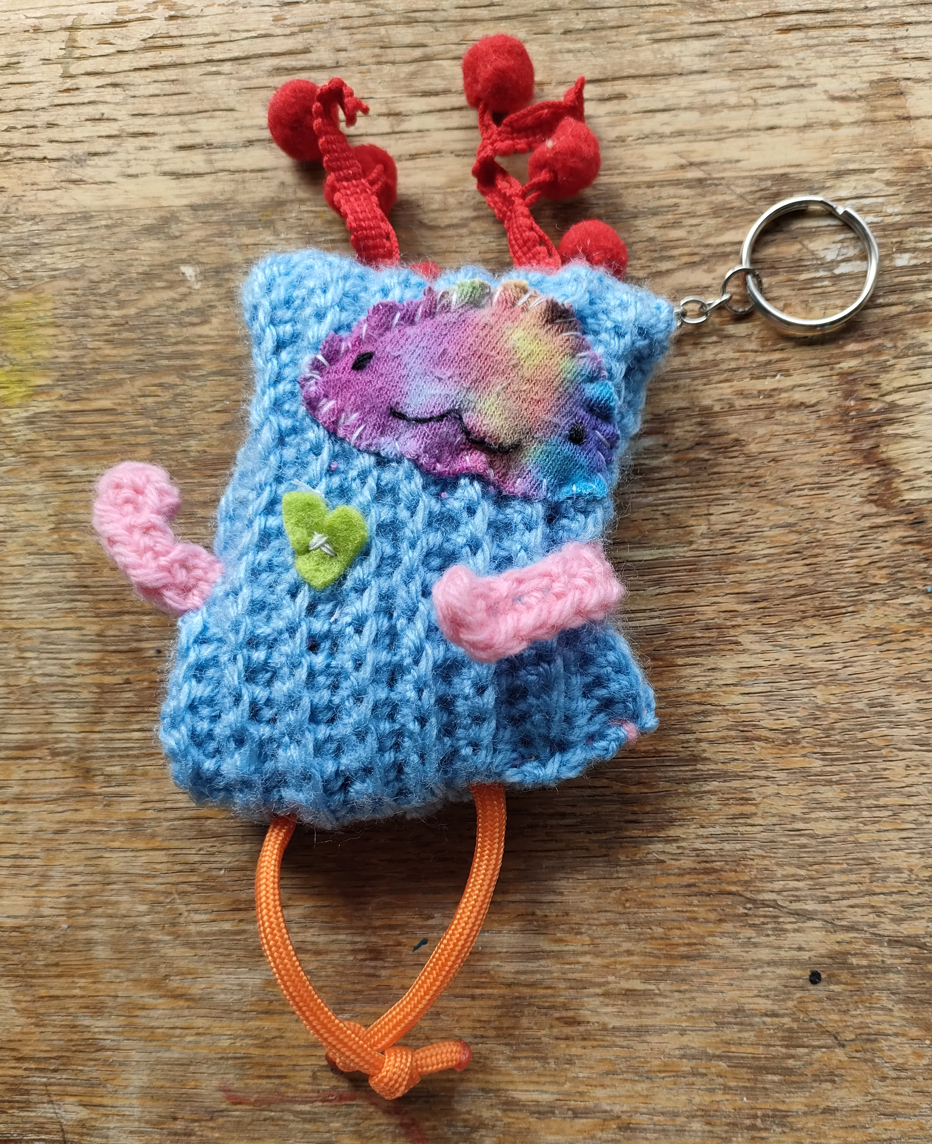 Handmade keyring of a crocheted blue creature with a friendly expression and multicoloured limbs, as well as a red felt heart.
